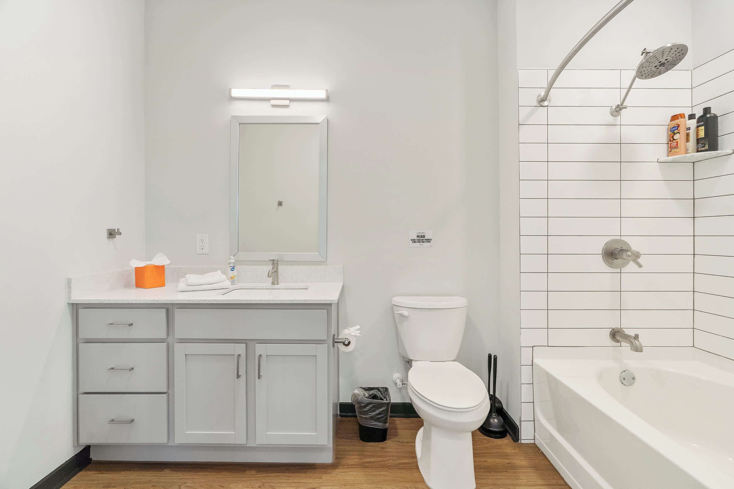 A modern bathroom with a white sink, mirror, and toilet, a shower with a handheld showerhead, and a bathtub.