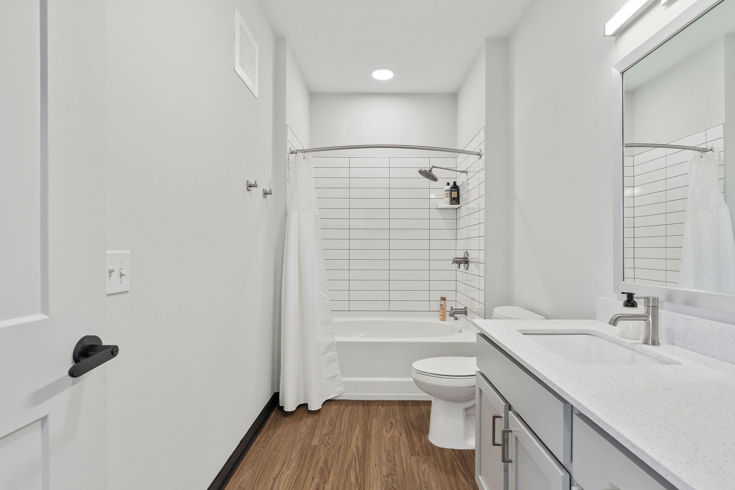 A modern bathroom with a shower, toilet, and sink, featuring white tiles and a wooden floor.