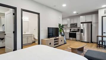 Une chambre d’hôtel moderne dotée d’un grand lit, d’une télévision, d’une table de chevet en bois et d’une kitchenette équipée d’un four à micro-ondes et d’un réfrigérateur.