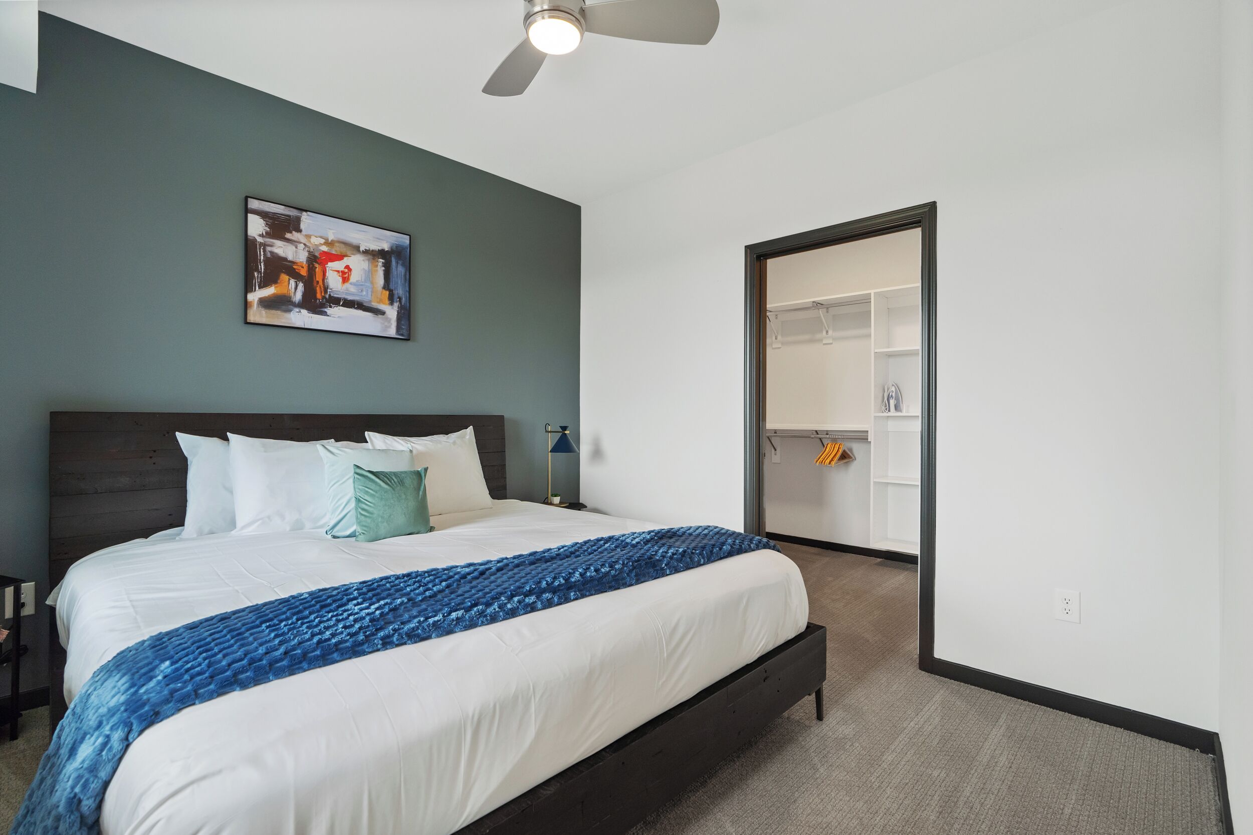 A bedroom with a bed, a ceiling fan, a painting, and a walk-in closet.