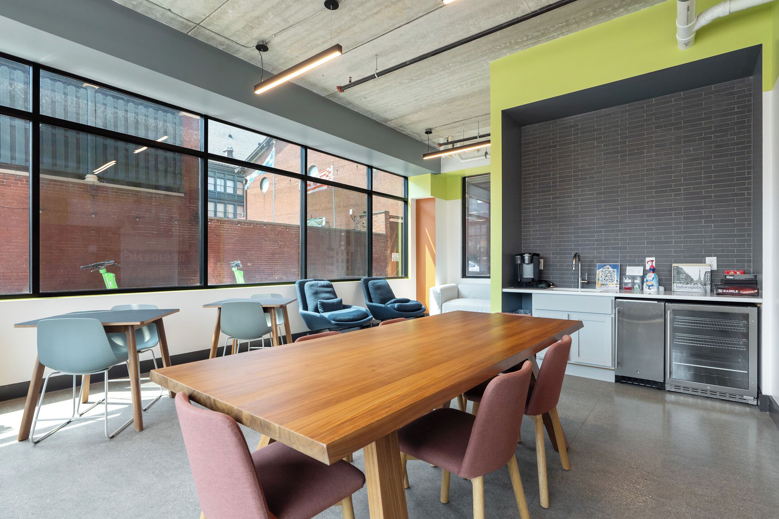 A conference room with a long wooden table, multiple chairs, a kitchenette, and large windows.