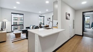 A modern kitchen with a central island, a dining area with a table and chairs, and a living room with a sofa and a coffee table. - CozySuites at Block20 (Indianapolis)