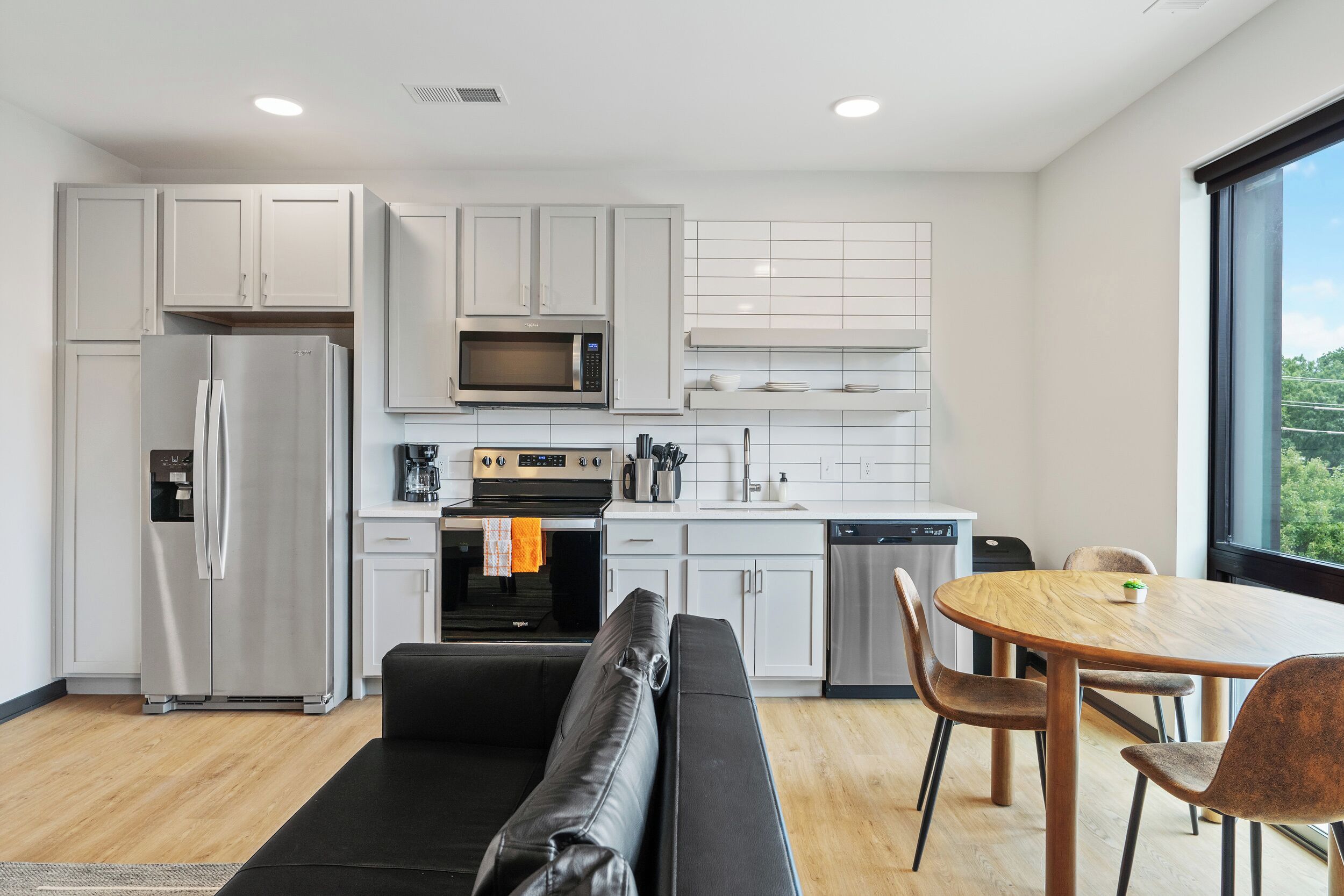 A modern kitchen with white cabinets, a stainless steel refrigerator, a microwave, and a dining area with a round wooden table and chairs.