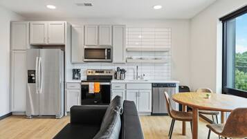 A modern kitchen with white cabinets, a stainless steel refrigerator, a microwave, and a dining area with a round wooden table and chairs.
