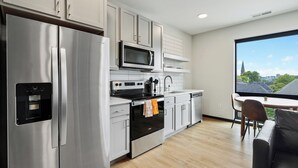 A modern kitchen with stainless steel appliances, a microwave, and a view of a cityscape through a large window. - CozySuites at Block20 (Indianapolis)