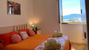 A bedroom with a wooden headboard, orange bedding, and a view of the sea through a window. - Casa Marea Sperlongaresort (Sperlonga)