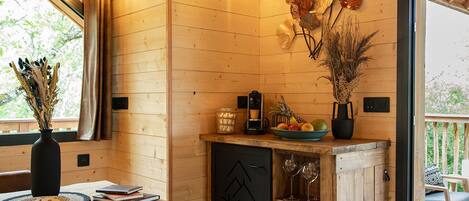 Interior acogedor de una cabaña de madera con una mesa de comedor, un aparador con cristalería y vistas al exterior.