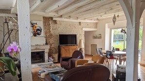 A cozy living room with a fireplace, leather sofas, a television, and a dining area with a view of the garden.