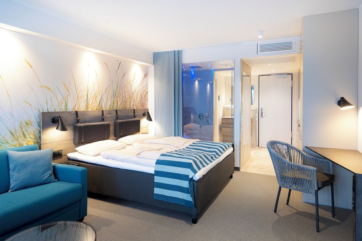 A modern hotel room with a bed, a desk, a chair, and a sofa.
