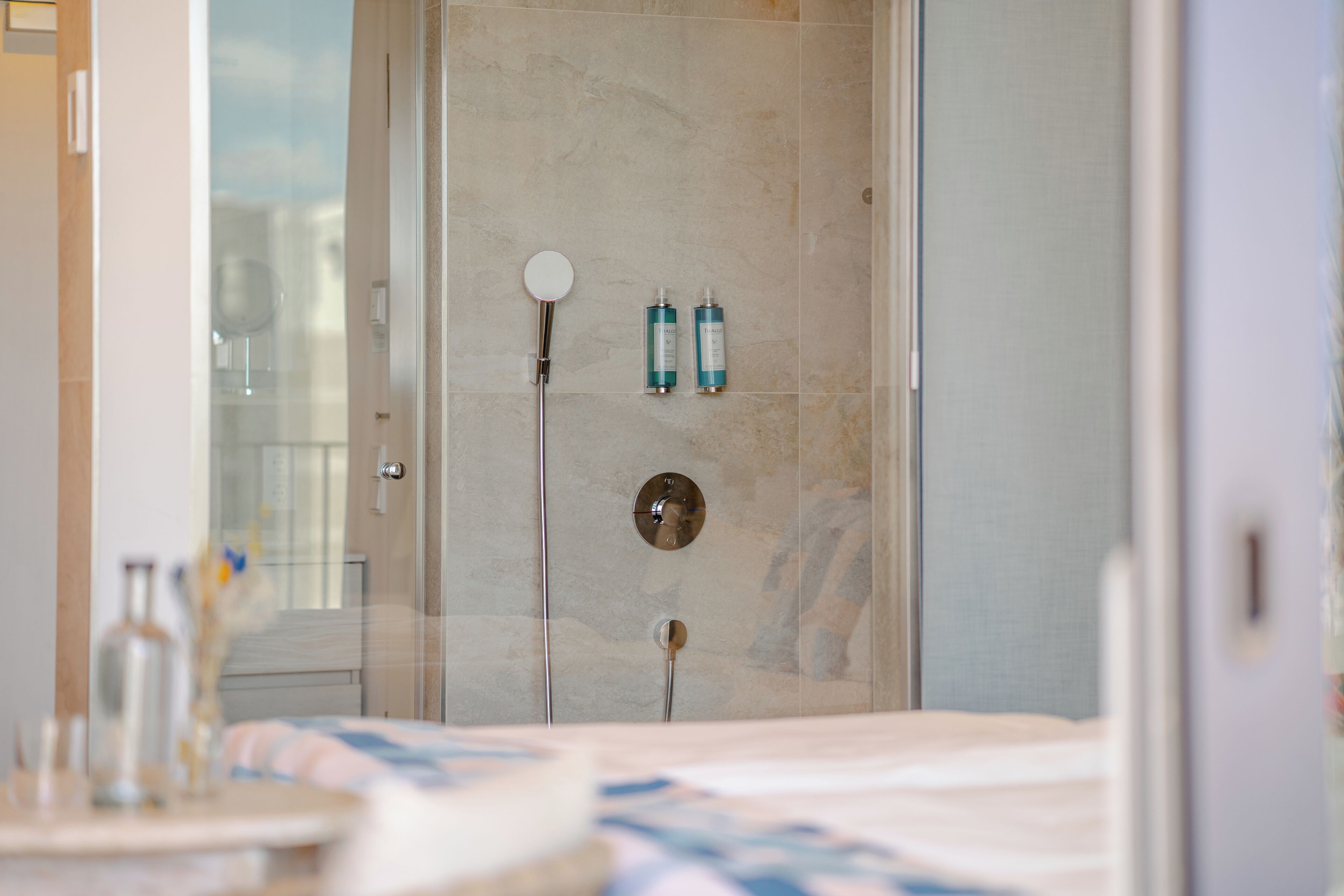 A modern bathroom with a glass shower enclosure, a round mirror, and two bottles of shampoo on the wall.