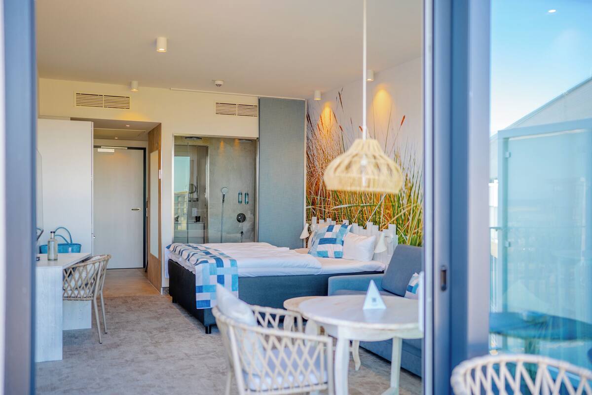 A modern hotel room with a bed, seating area, and a view through a glass door.