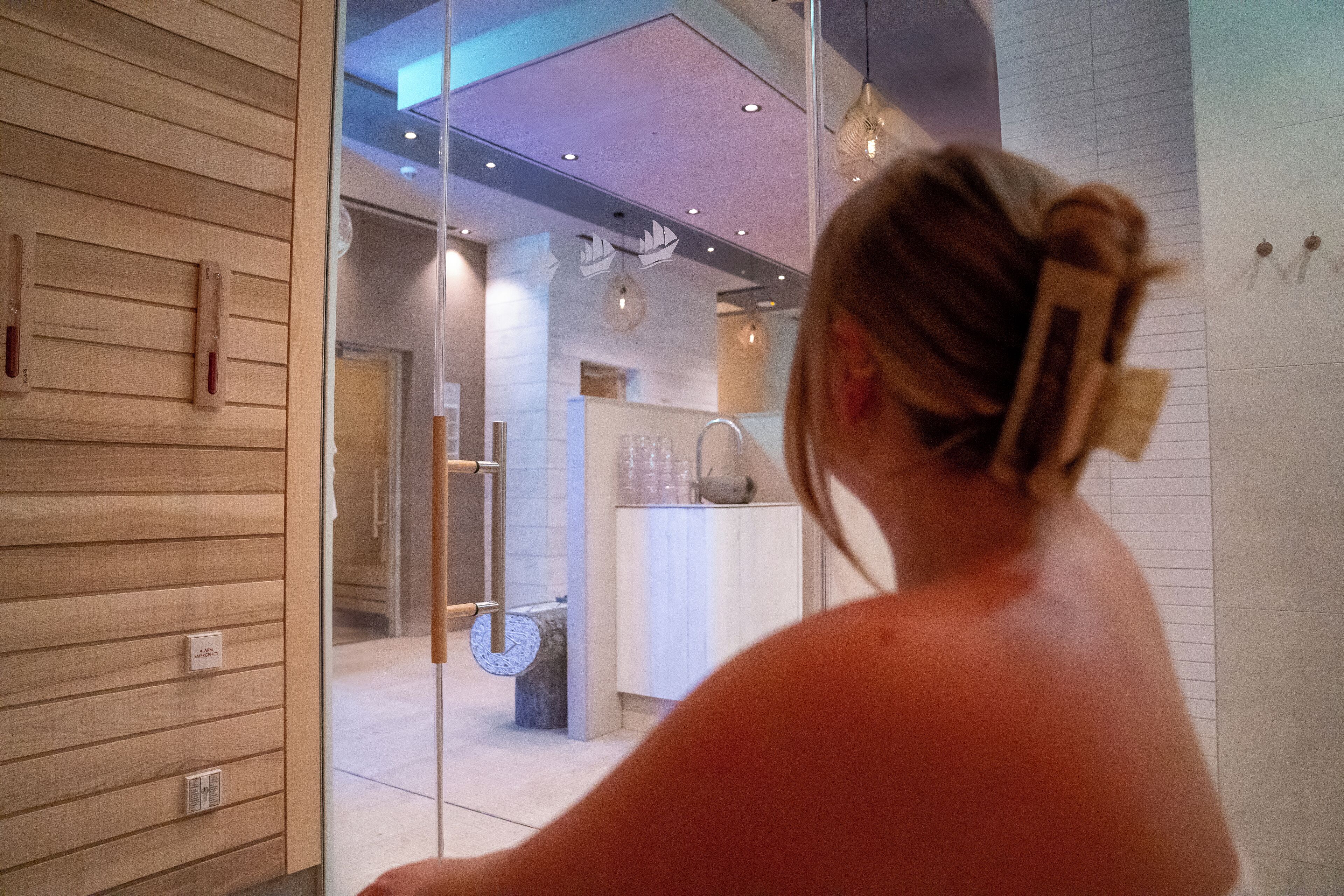 Un intérieur moderne avec un lambris en bois, une porte en verre donnant sur une salle de bain et des luminaires suspendus.