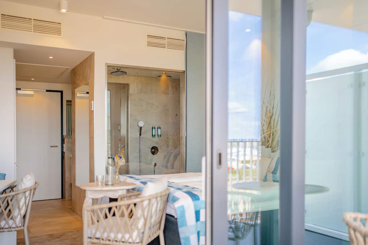 A modern bathroom with a glass shower enclosure, a small table with chairs, and a view of the outdoors.