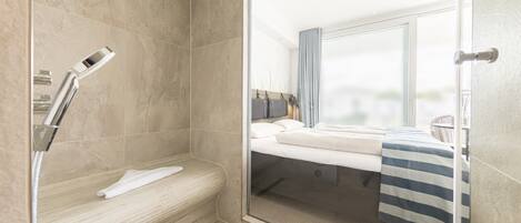 A modern bathroom with a glass shower enclosure, a bench, and a bed with a striped towel.
