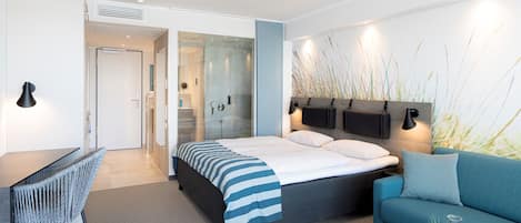 Une chambre d’hôtel moderne équipée d’un lit, d’un canapé, d’un bureau et d’une douche à parois de verre.