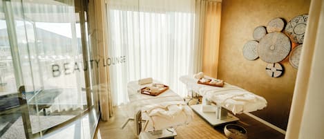 A spa room with two treatment beds, a glass wall with a view, and a wall decorated with circular plates.