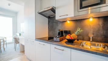 Une cuisine moderne avec des meubles blancs, un four à micro-ondes en acier inoxydable et un panier de fruits posé sur le plan de travail.
