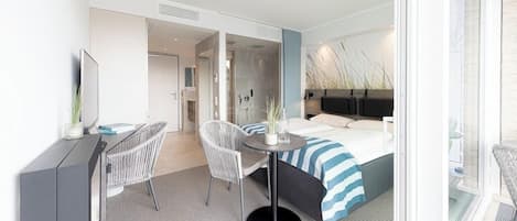 Una habitación de hotel moderna con una cama, un escritorio, dos sillas, una mesita pequeña y un ventanal grande.