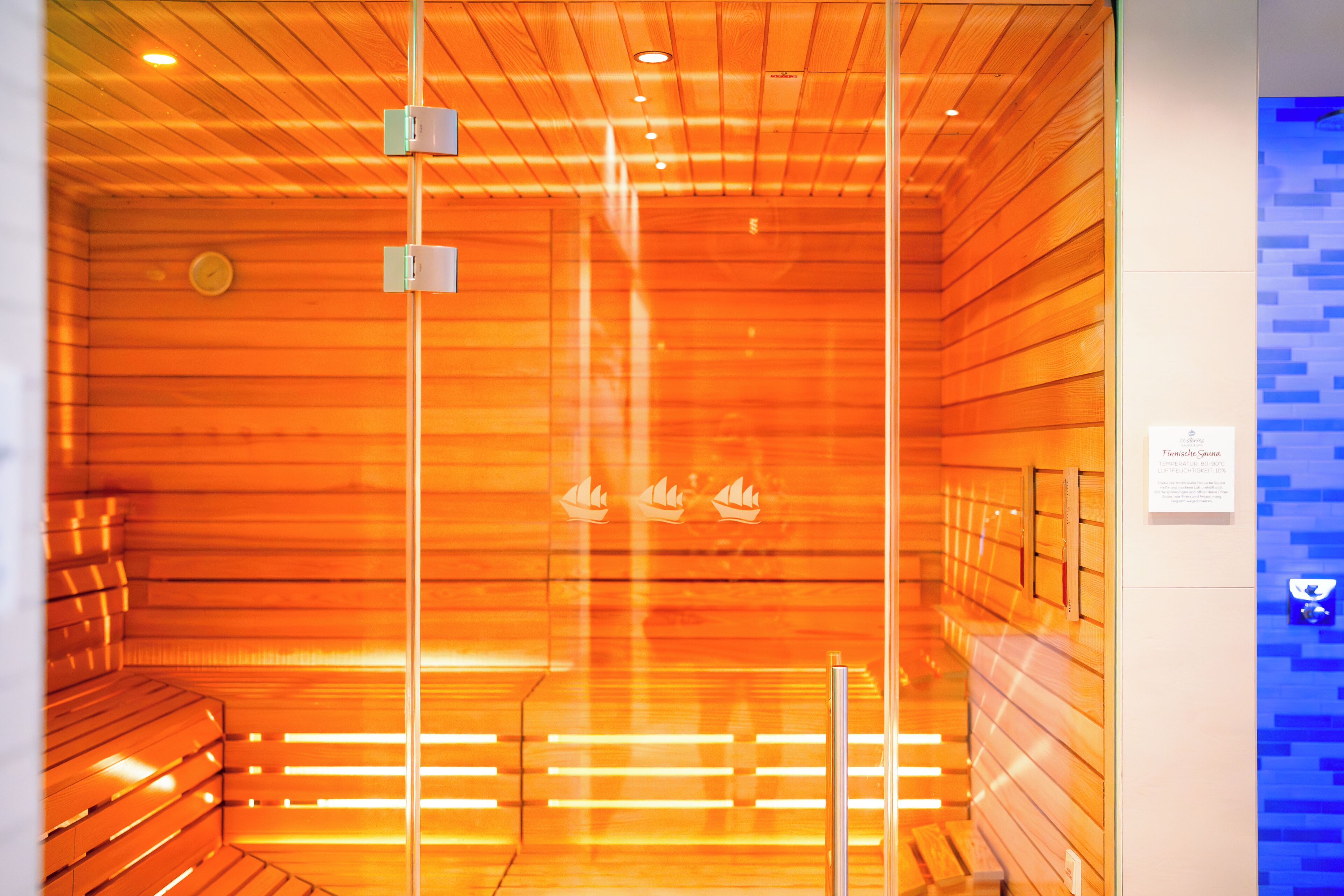 En sauna med trælameller og bænke, et synligt temperaturregulering og et skilt med information om saunaen.