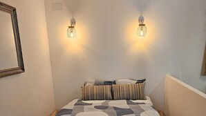 A neatly made bed with a patterned bedspread, two wall-mounted lamps, and a mirror on the left.