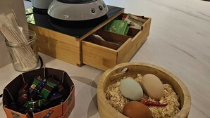 A kitchen with a coffee maker, a wooden box with tea bags, a basket with chocolates, and a wooden bowl with eggs.