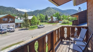A wooden deck with chairs, a view of a street with parked cars, and houses with green roofs.