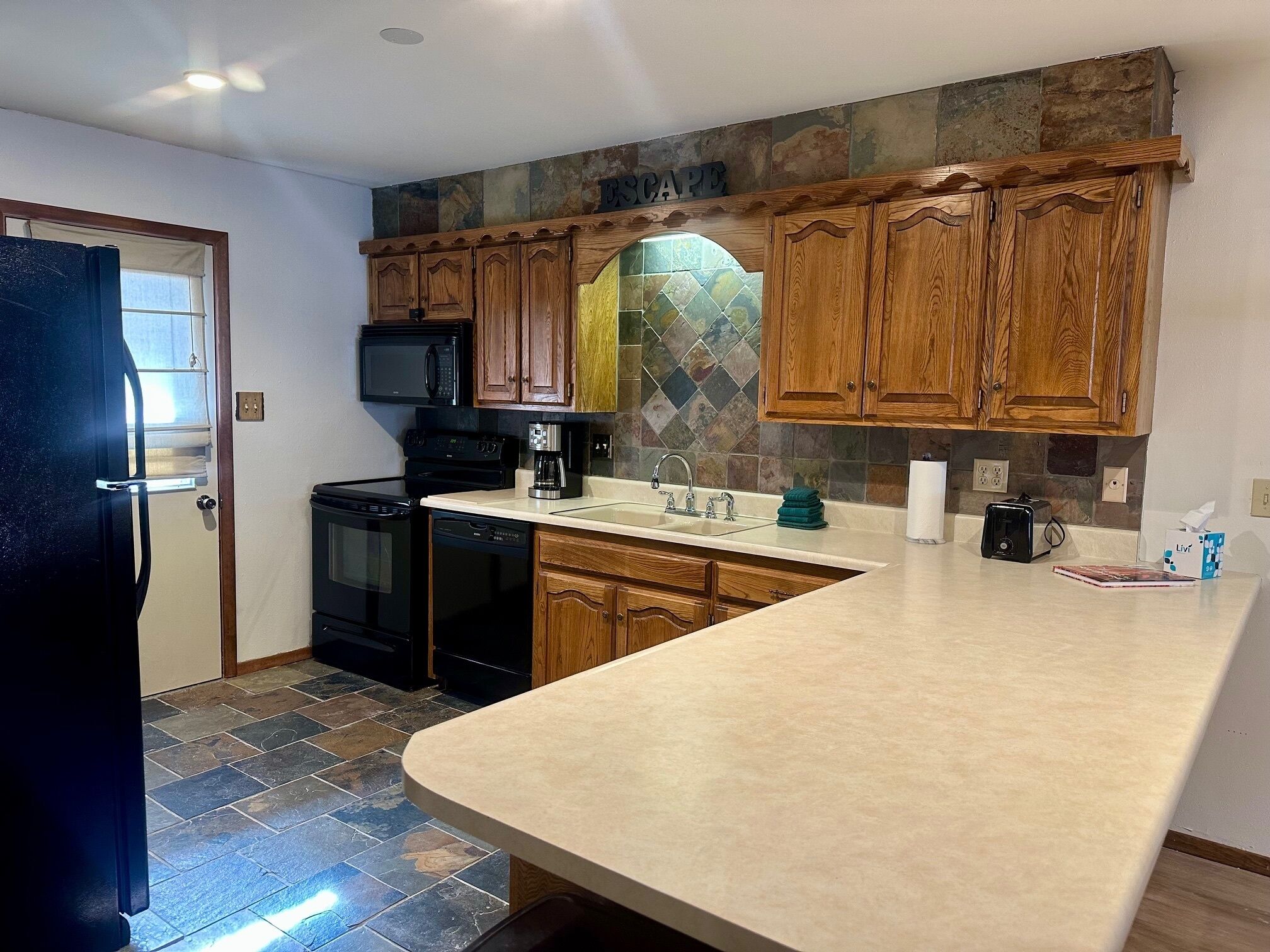 A kitchen with wooden cabinets, a microwave, a coffee maker, and a stone backsplash.