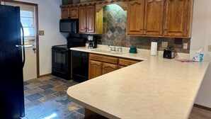 A kitchen with wooden cabinets, a microwave, a coffee maker, and a stone backsplash.