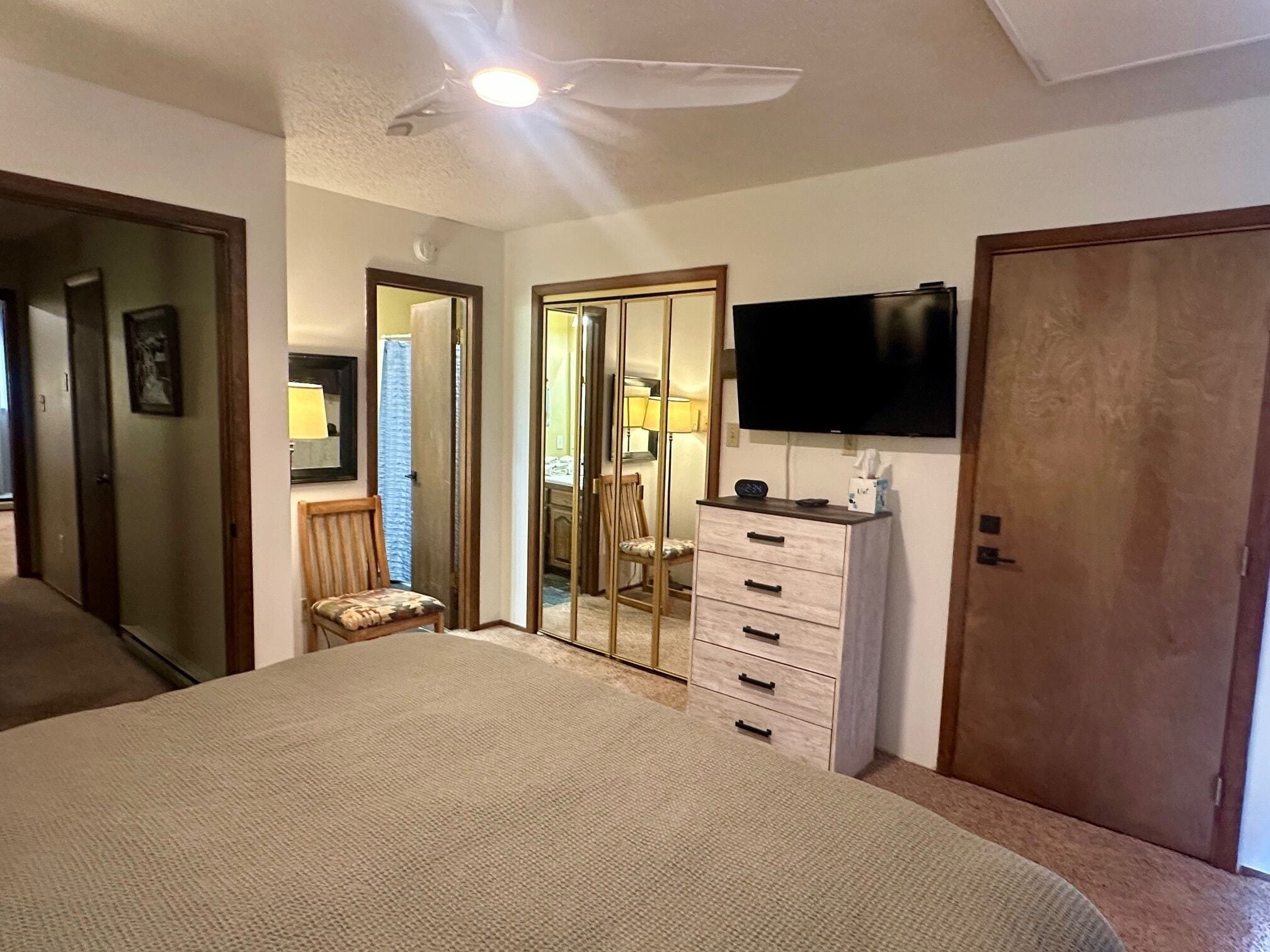 Een slaapkamer met een bed, een dressoir, een televisietoestel en een deur naar een andere kamer.