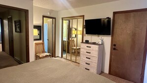 A bedroom with a bed, a dresser, a television, and a door leading to another room.