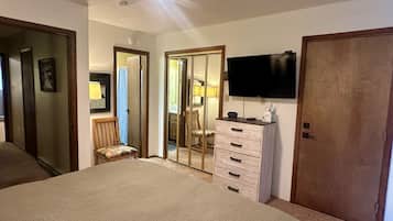 Een slaapkamer met een bed, een dressoir, een televisietoestel en een deur naar een andere kamer.