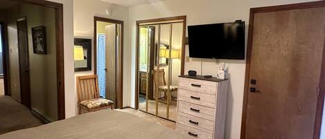 A bedroom with a bed, a dresser, a television, and a door leading to another room.