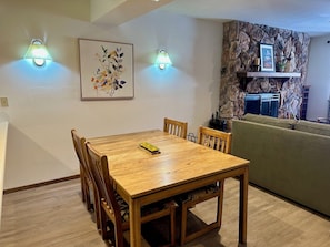 Un coin repas avec une table et des chaises en bois, deux lampes fixées au mur, une œuvre d’art florale encadrée et un mur décoratif en pierre.