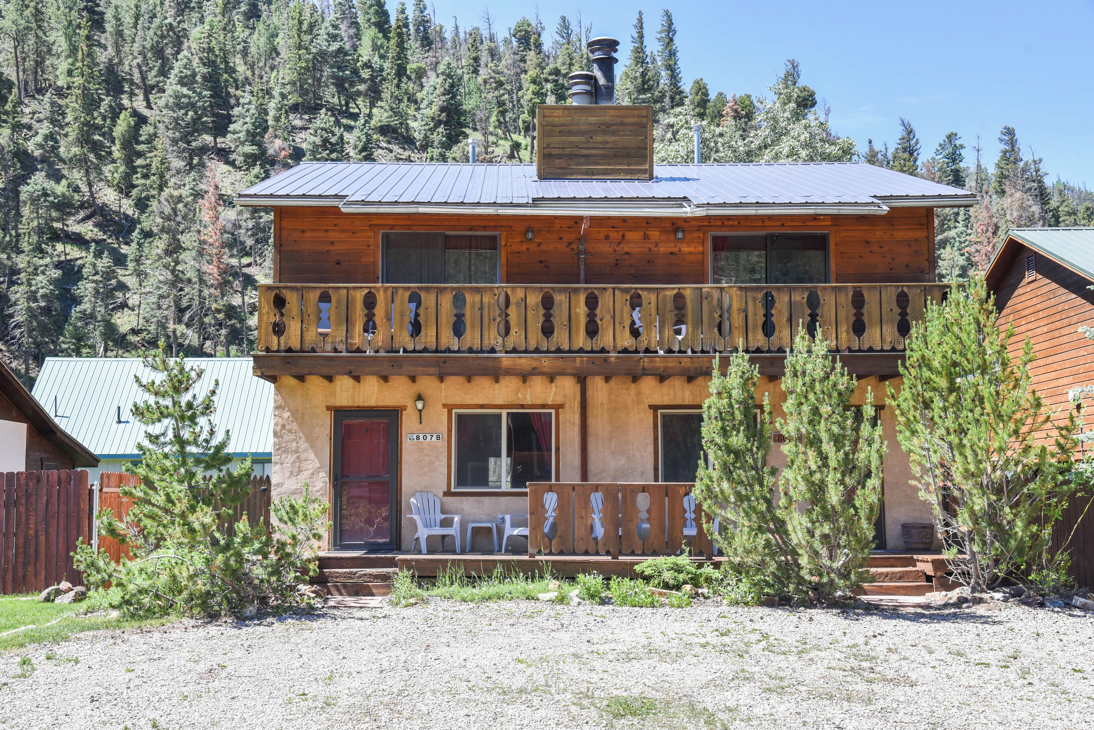 A two-story wooden cabin with a balcony, a chimney, and a front porch with chairs.