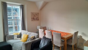 Ein gemütliches Wohnzimmer mit einer Couch, Sesseln, einem Esstisch und Blick auf eine Baustelle vor dem Fenster.