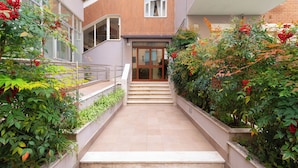A staircase leading to a building entrance with a glass door, surrounded by lush greenery and plants. - YourHome - Domus Apartment (Sorrento)