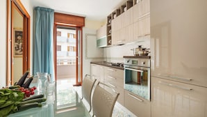 A modern kitchen with a dining table, chairs, and a view of the outside balcony. - YourHome - Domus Apartment (Sorrento)
