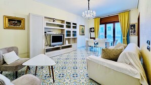 A living room with a TV, sofa, chairs, and a patterned floor. - YourHome - Domus Apartment (Sorrento)