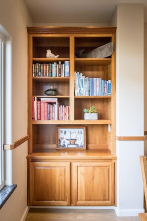 Een houten boekenkast met boeken, decoratieve objecten, een klein plantje en een ingelijst beeld op een onderste plank.