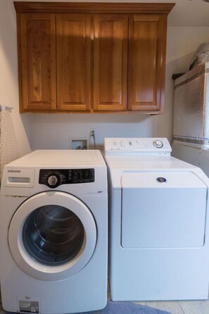 A laundry area with a Samsung VRT washer and dryer, wooden cabinets above, and a window with a mesh screen.