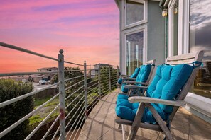 A balcony with two wooden chairs and a view of the cityscape during sunset.