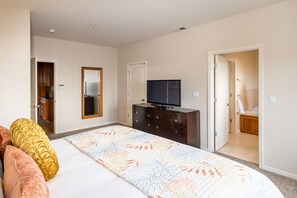 Een slaapkamer met een bed, een dressoir, een televisie, en een zichtbare badkamer door een open deur.
