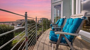 Un balcon avec deux chaises en bois et une table, d’où l’on peut admirer la vue sur la ville au coucher du soleil.