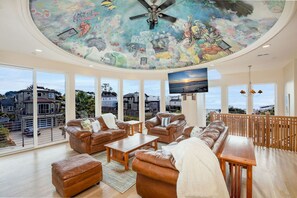 A spacious living room with leather sofas, a wooden coffee table, and a ceiling mural.