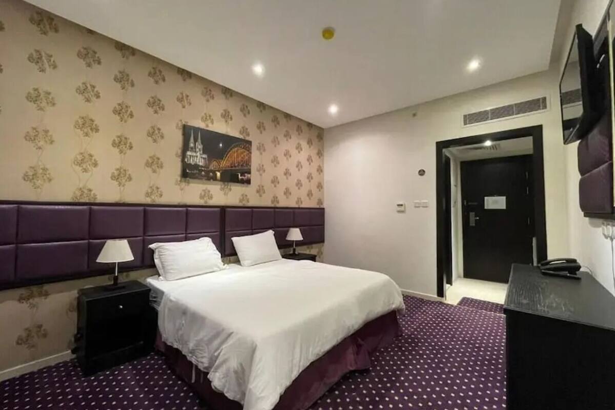 A hotel room with a bed, two bedside tables with lamps, a wall-mounted TV, and a door.