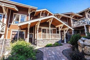 Un immeuble à plusieurs étages, doté de fondations en pierre, d’une façade en bois et d’un porche couvert avec des balustrades blanches.