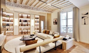 A modern living room with a white sofa, a coffee table, and a bookshelf filled with decorative items. - A LUXURIOUS RETREAT WHERE HISTORY MEETS CONTEMPORARY DESIGN AT RUE DU TEMPLE  (Paris)