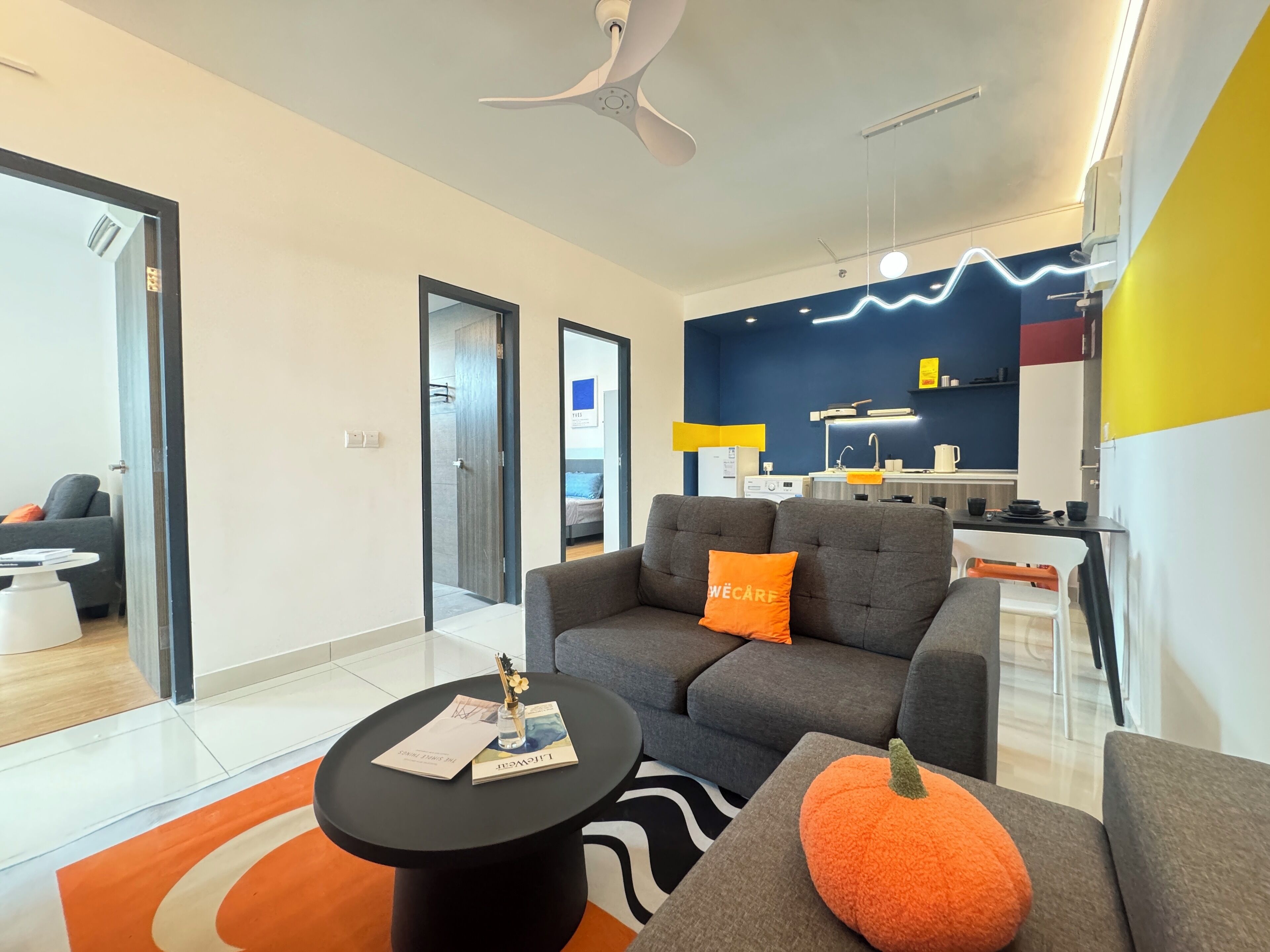 A modern living room with a grey sofa, a black coffee table, and a pumpkin decoration. There is a kitchen area with a blue wall and a white refrigerator.