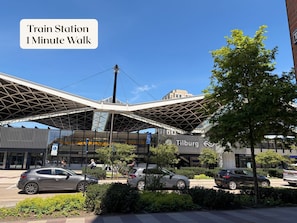 A modern train station with a distinctive roof structure, a clear sky, and a few pedestrians.