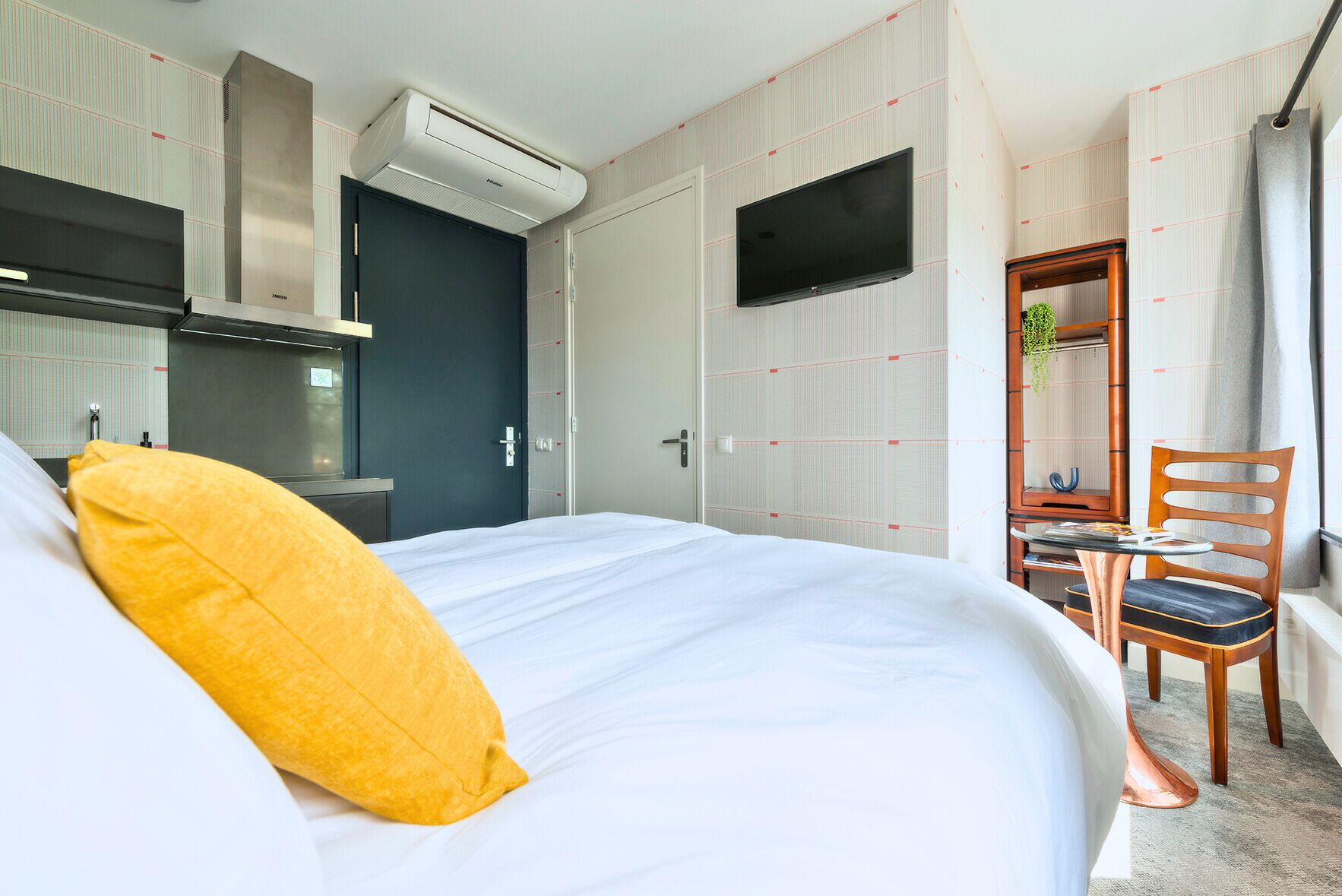 Een hotelkamer met een bed, bureau, stoel, televisie en airconditioning.